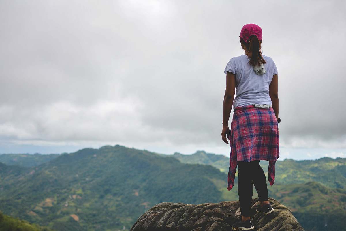 people woman standing on mountain peak facing green mountains at daytime person