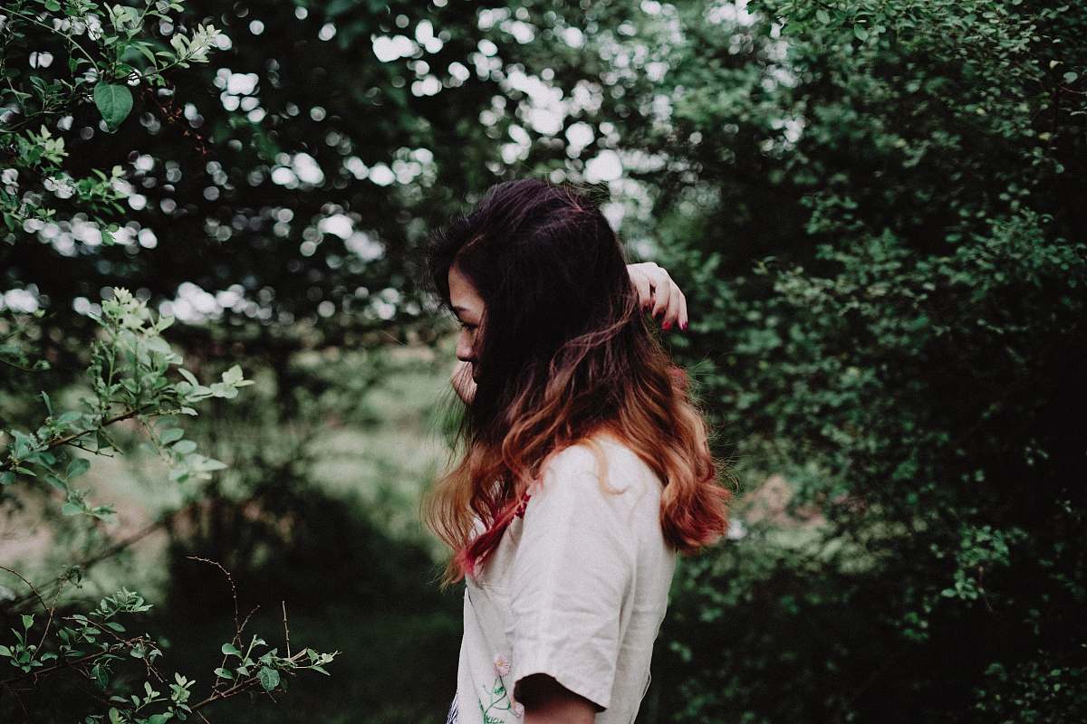 This captivating image features a woman deeply immersed in nature, gazing thoughtfully at the vibrant plants around her in a serene woodland setting. The interplay of light filtering through the trees highlights her connection with the environment, making it a perfect visual for topics related to mindfulness, nature appreciation, and outdoor lifestyle. Ideal for use in blogs, articles, or marketing materials focused on wellness, environmental conservation, or personal growth.