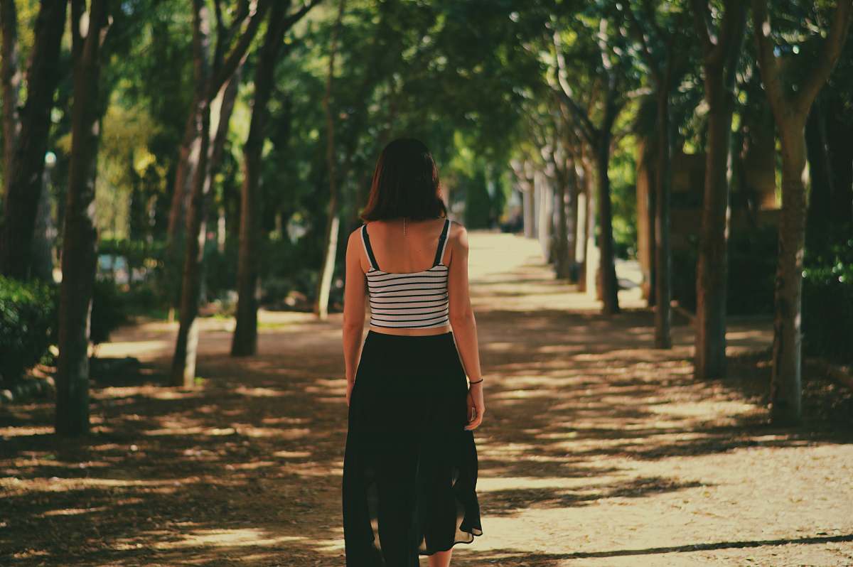 woman woman walking in between trees path