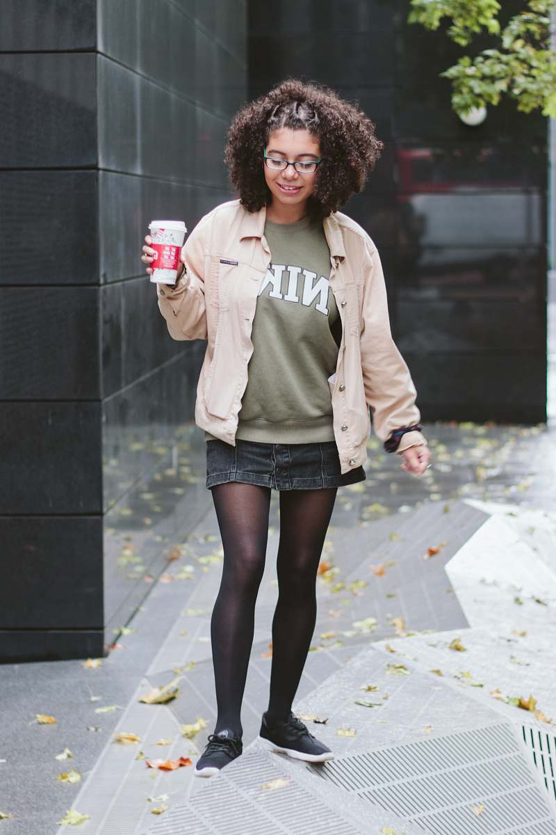 people woman wearing beige button-up collared long-sleeved shirt standing near black wall person