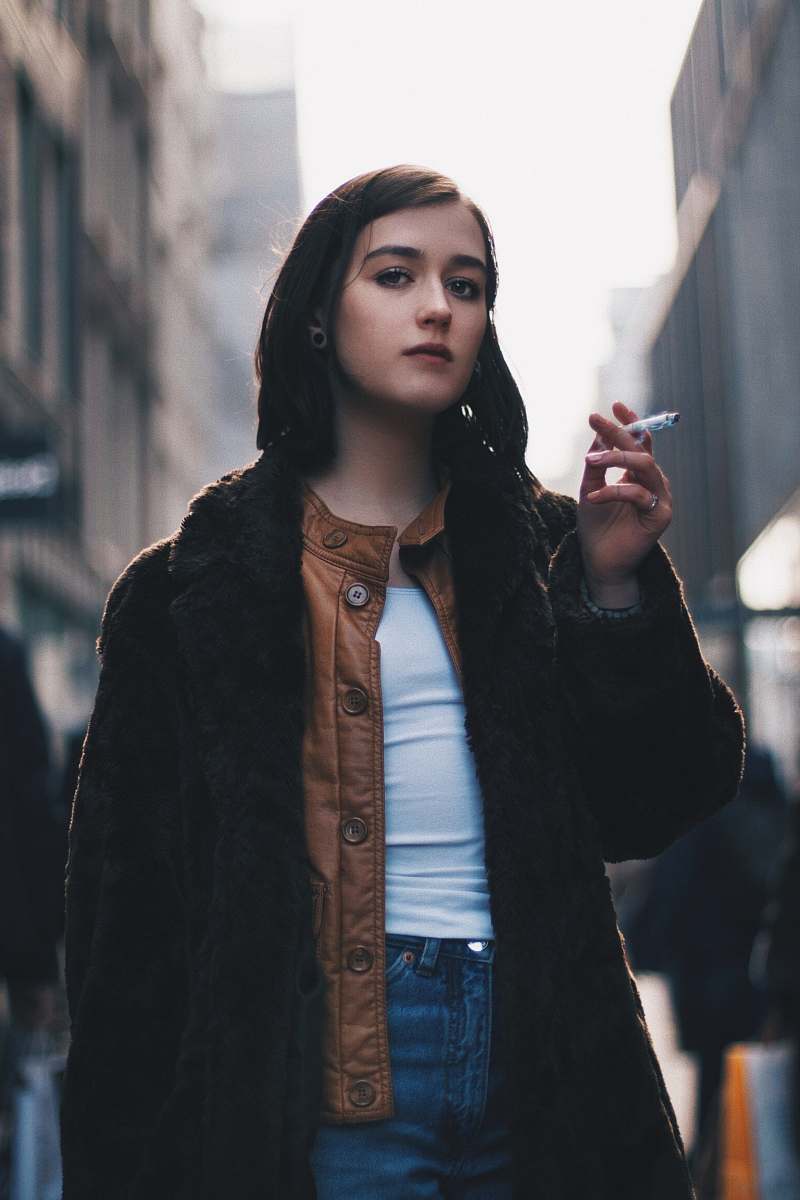 people woman wearing black coat and holding cigarette stick during daytime person
