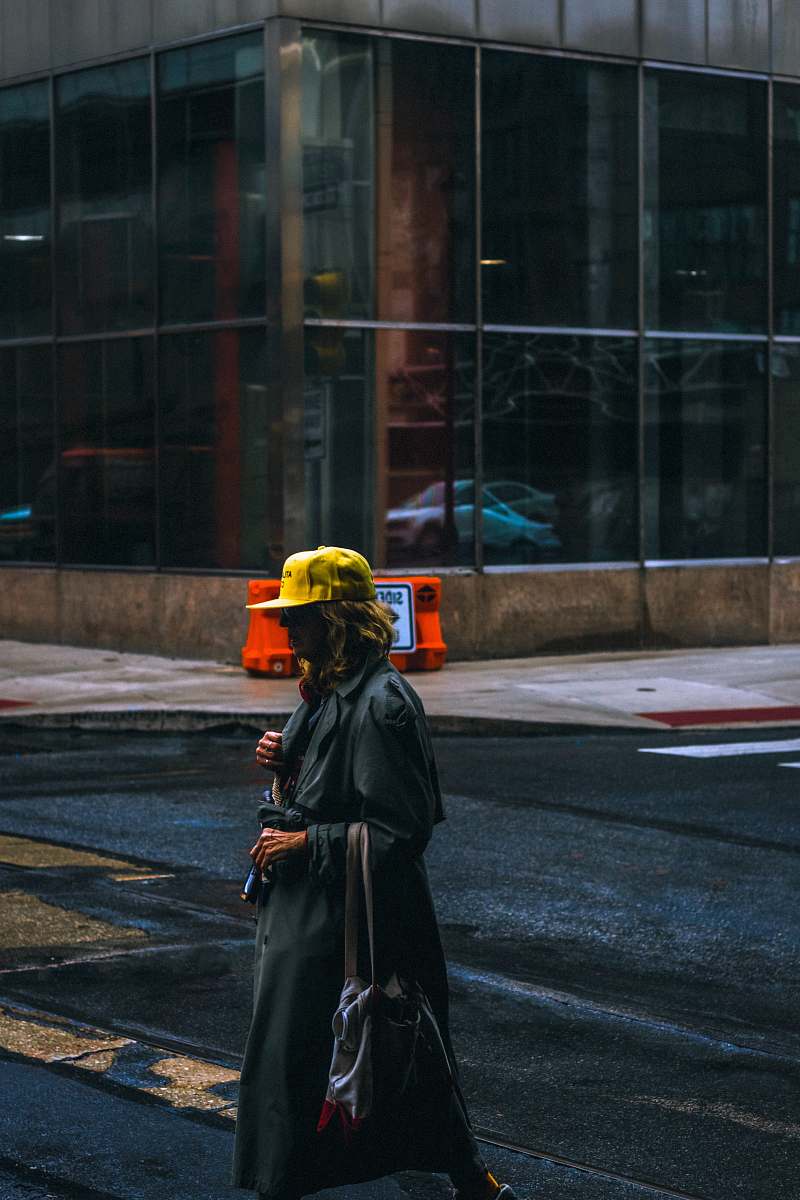 people woman wearing black trench coat and yellow cap walking on street person