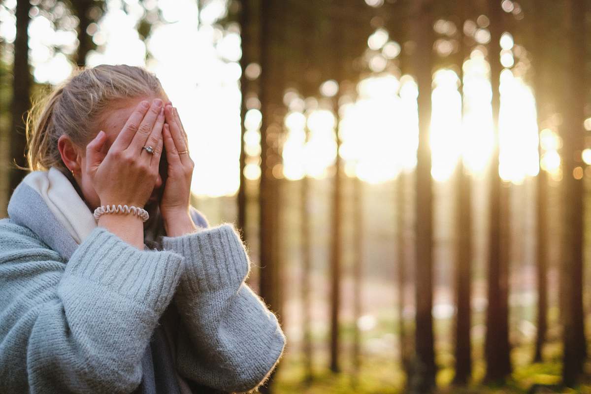 people woman wearing gray coat with hands on her face during daytime person