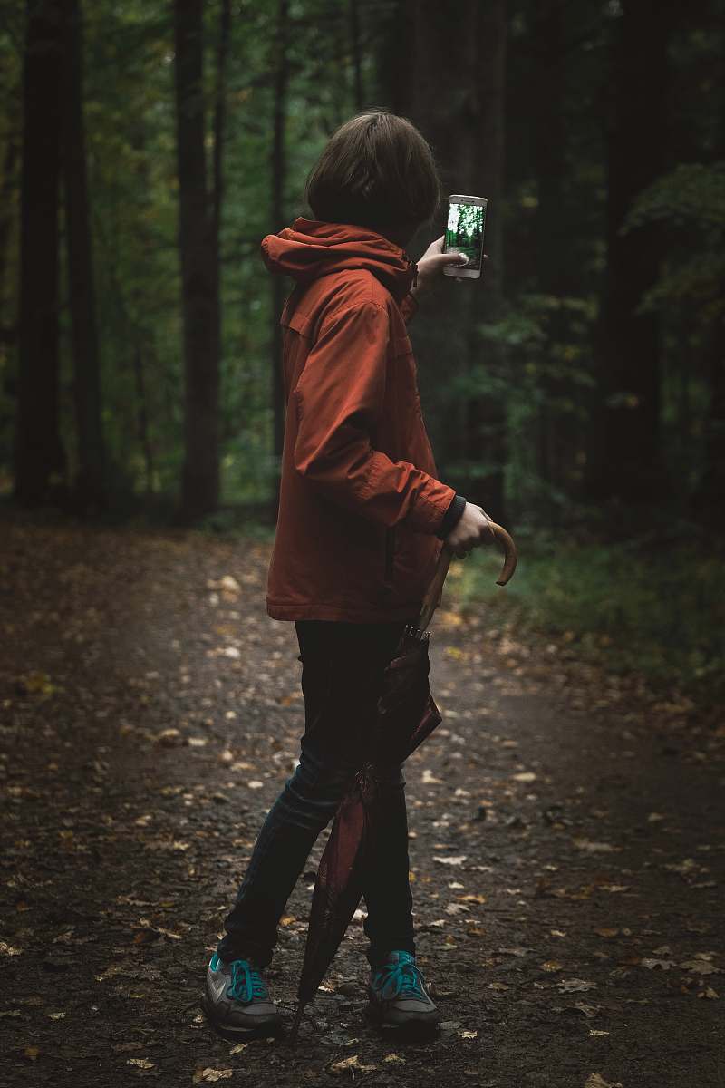 person woman wearing red hoodie holding smartphone near green leafed tree people