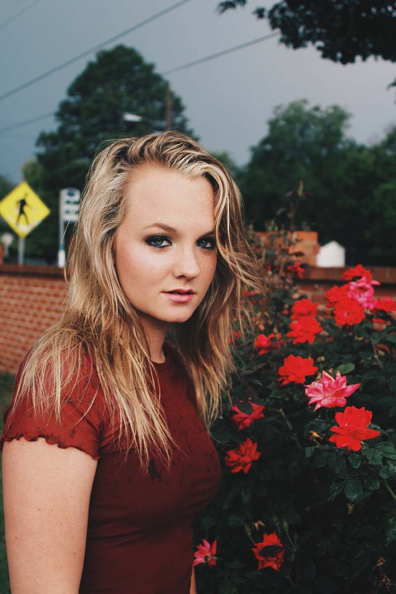 person woman wearing red shirt standing near red petaled flower people