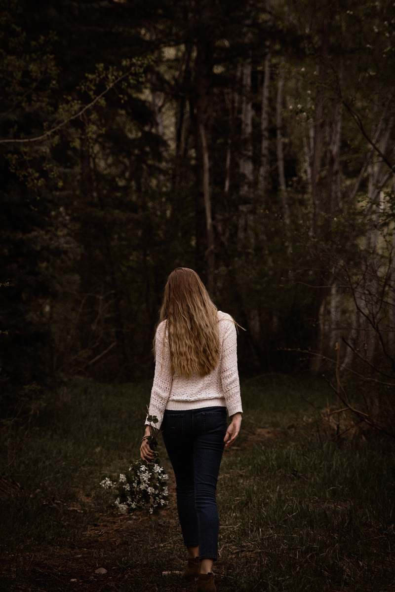 people woman wearing white sweater and black pants walking near trees person