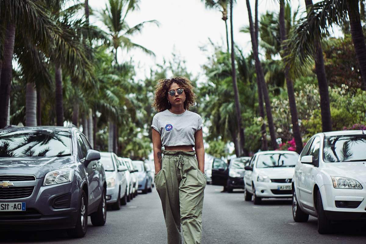 people woman with hands on pocket walking between vehicles on road during daytime person