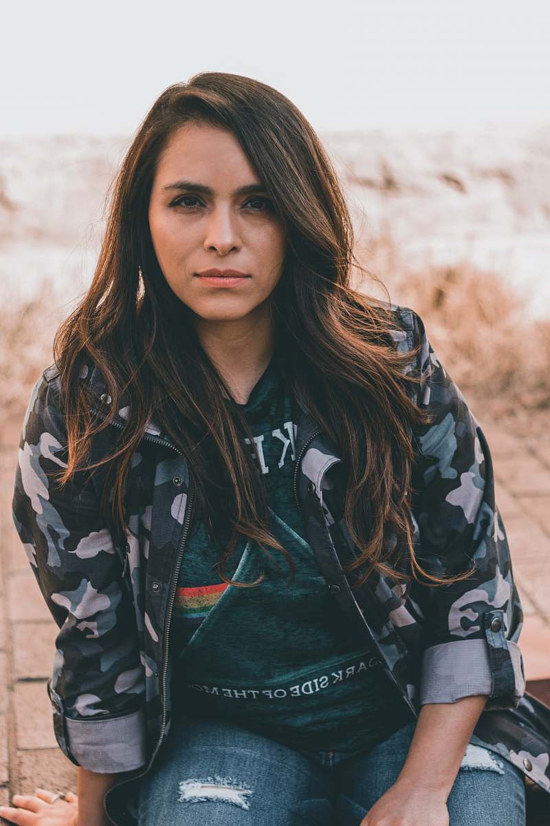 people women's black, white, and green camouflage zip-up jacket sitting on concrete floor person
