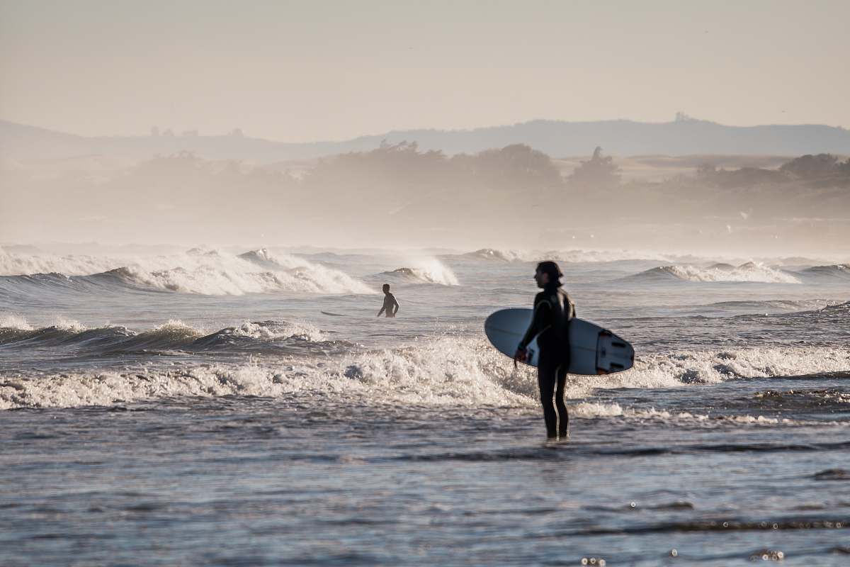 sea person holding white surfboard standing on body of water under gray sky during daytime surfboard