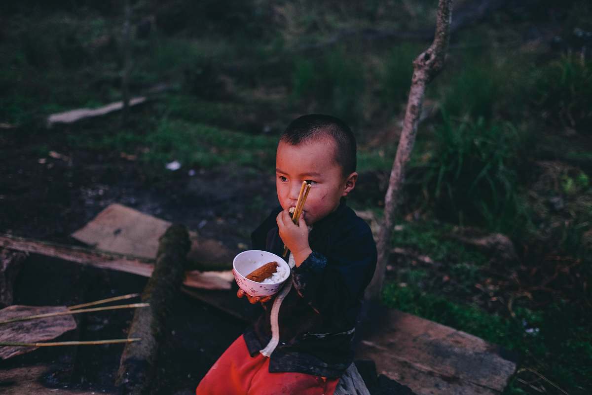 human boy earring food while holding round white bowl with pair of chopsticks person