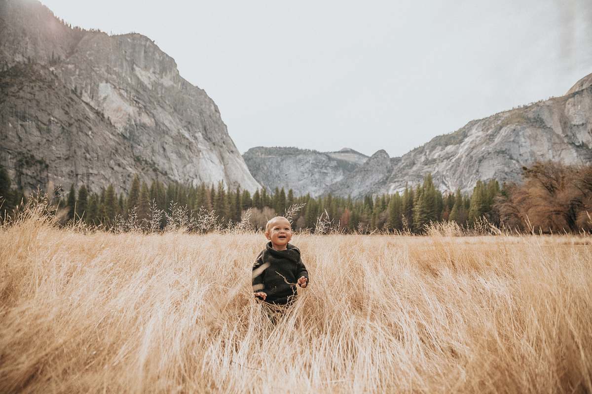 grass boy in black jacket stand on brown grass near mountain human