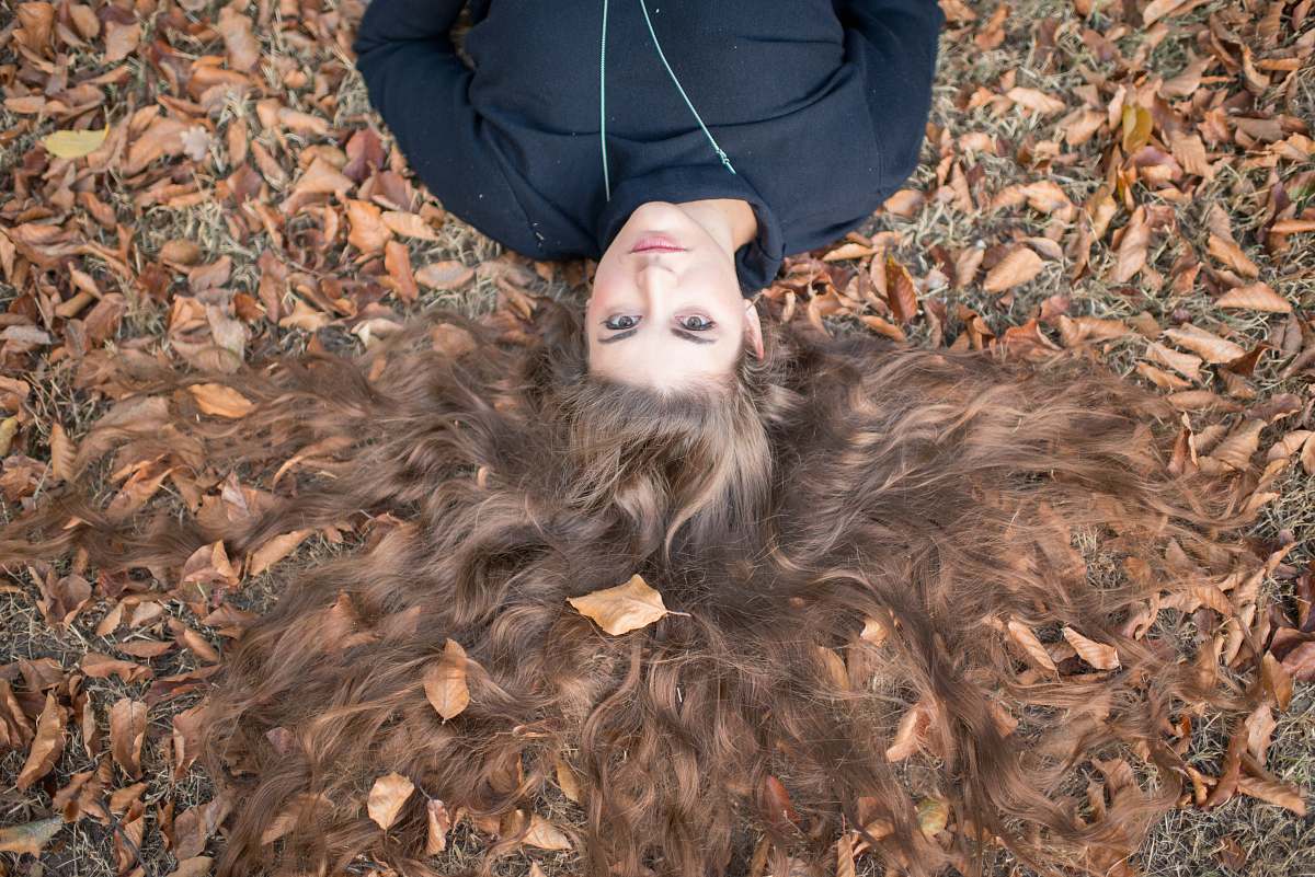 person flay lay photography of brown long-haired woman wearing black crew-neck top laying on field with dry leaves human