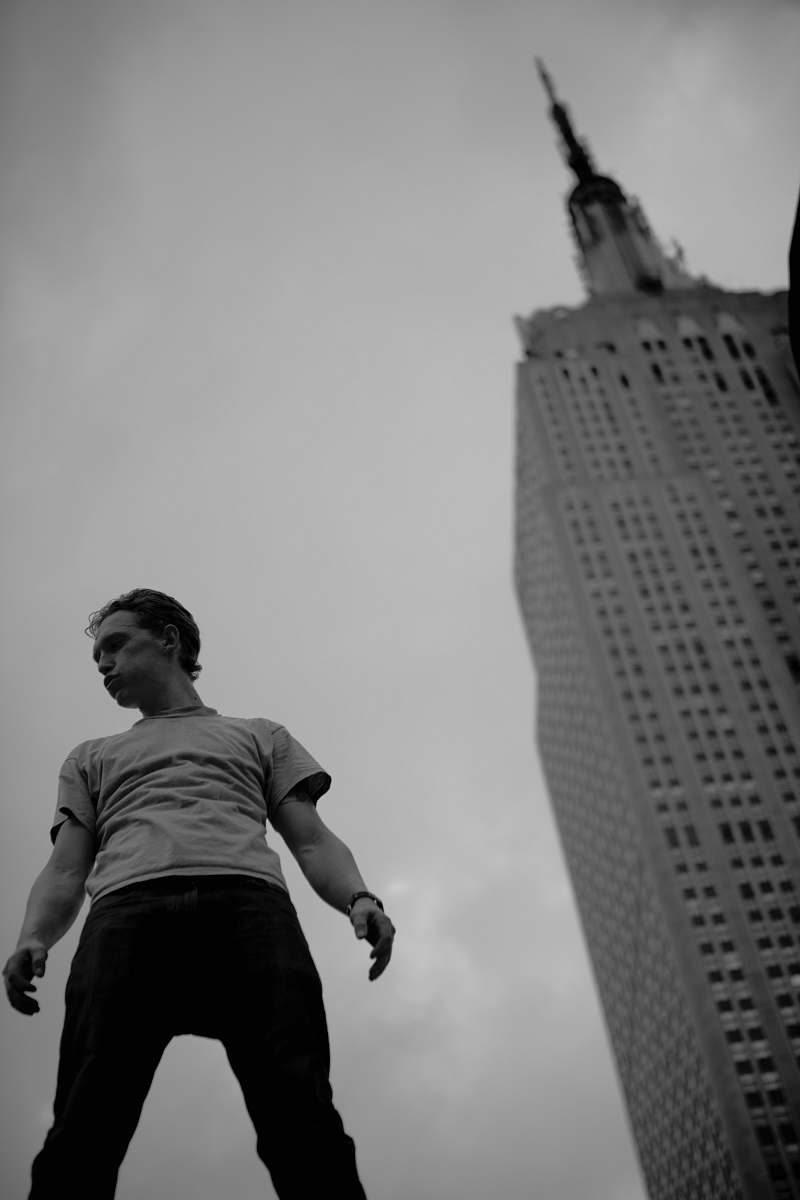 human grayscale low-angle photo of man standing near building black-and-white