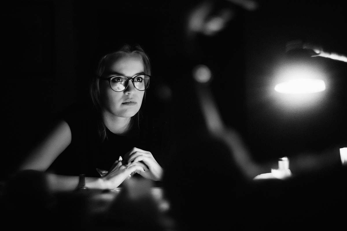 person grayscale photo of a woman wearing eyeglasses sitting in front of table black-and-white