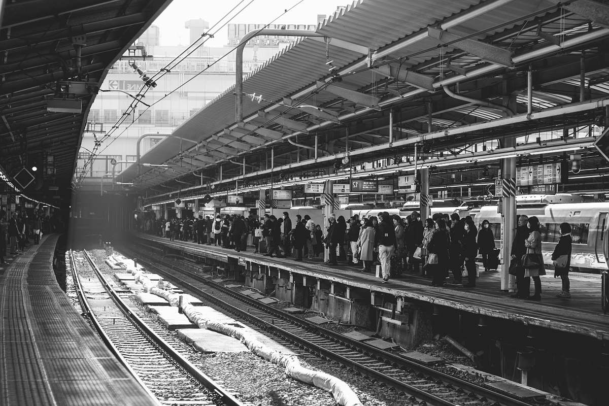 human grayscale photo of group of people walking in train station black-and-white