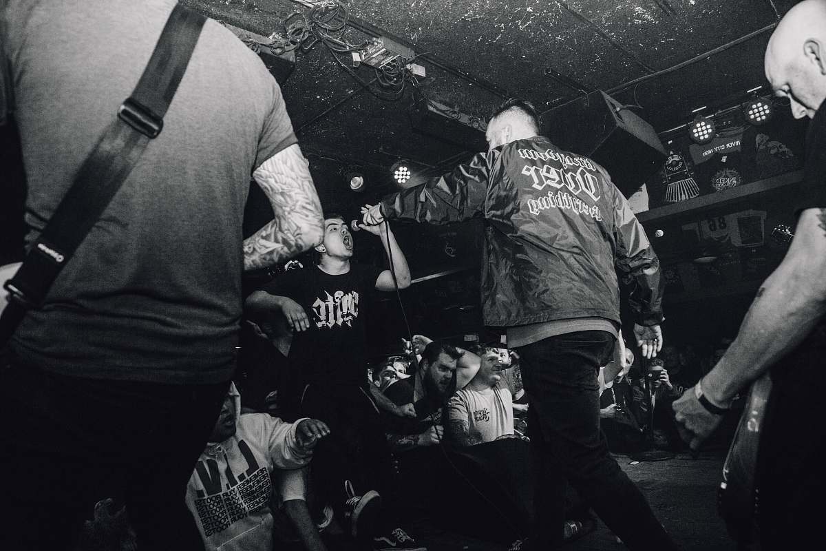 human grayscale photo of man holding microphone and surrounded by people person
