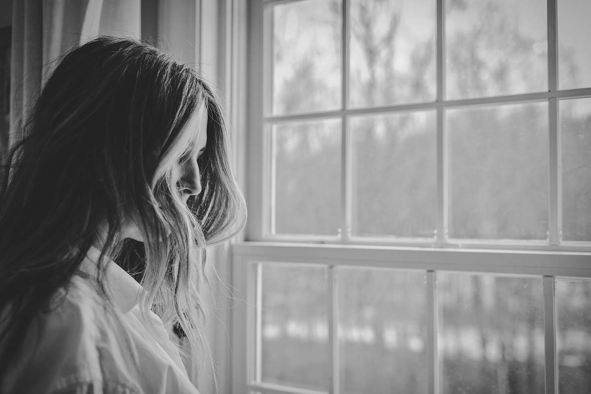 person grayscale photo of woman near window black-and-white