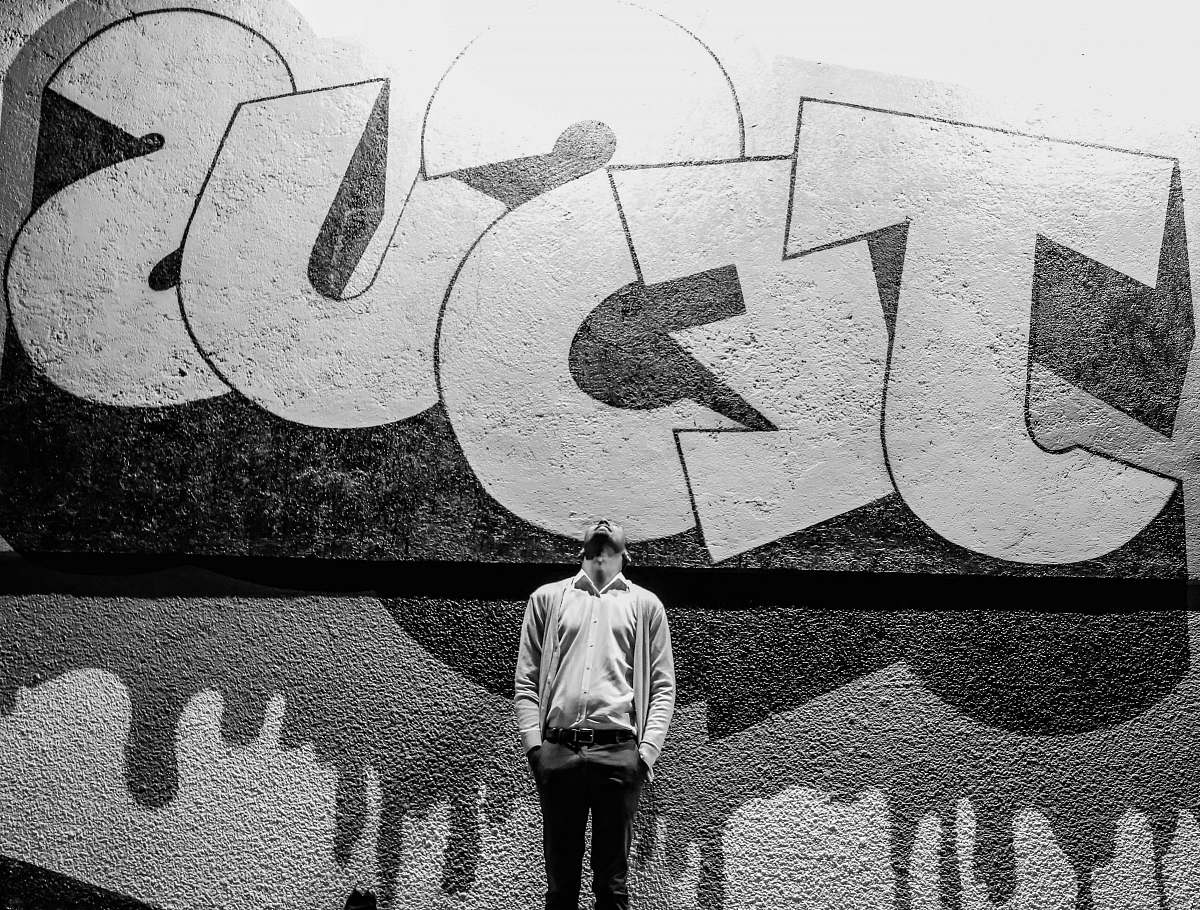 person grayscale photography of a man standing in front of a Jesus graffiti black-and-white