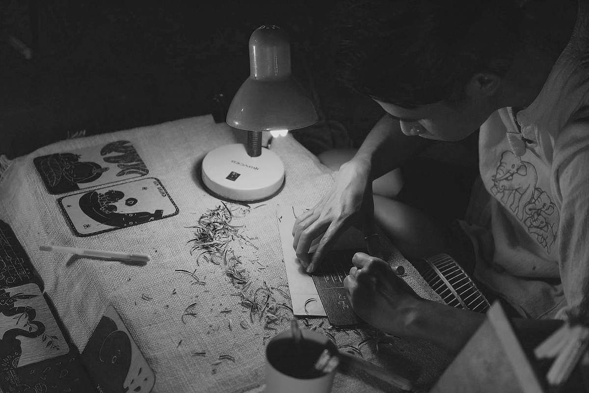 black-and-white grayscale photography of man writing on brown paper near turned on lamp grey