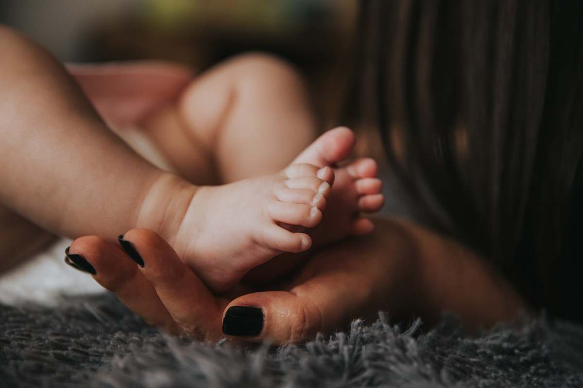 baby Infant's feet being held by a woman's hand with painted and manicured hands resting on a gray blanket newborn