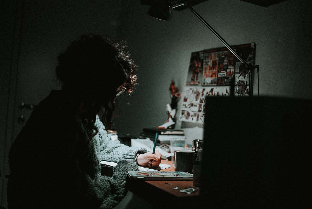 person low light photography of woman in gray knit sweatshirt writing on desk human