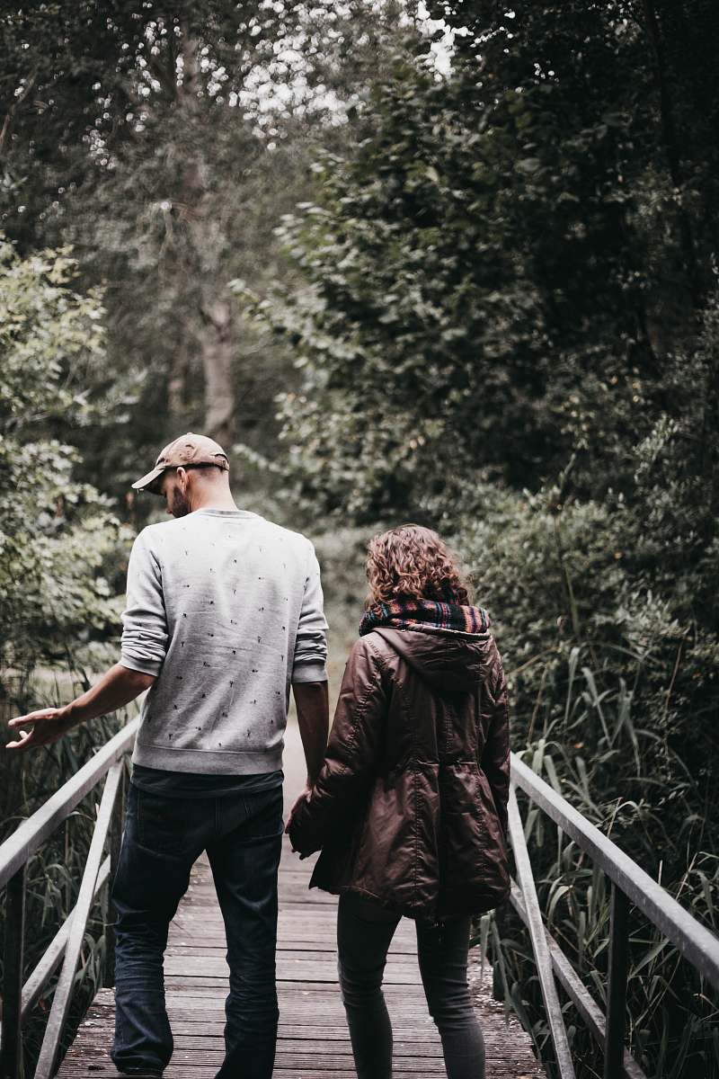 human man and woman holding hands walking on bridge during daytime person