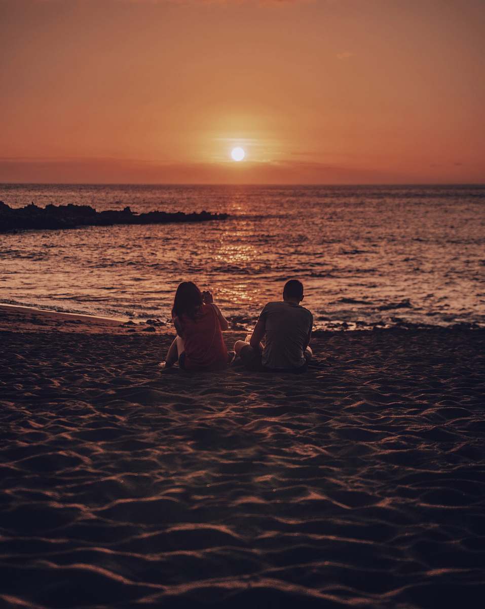 human man and woman sitting on beach during golden hour person
