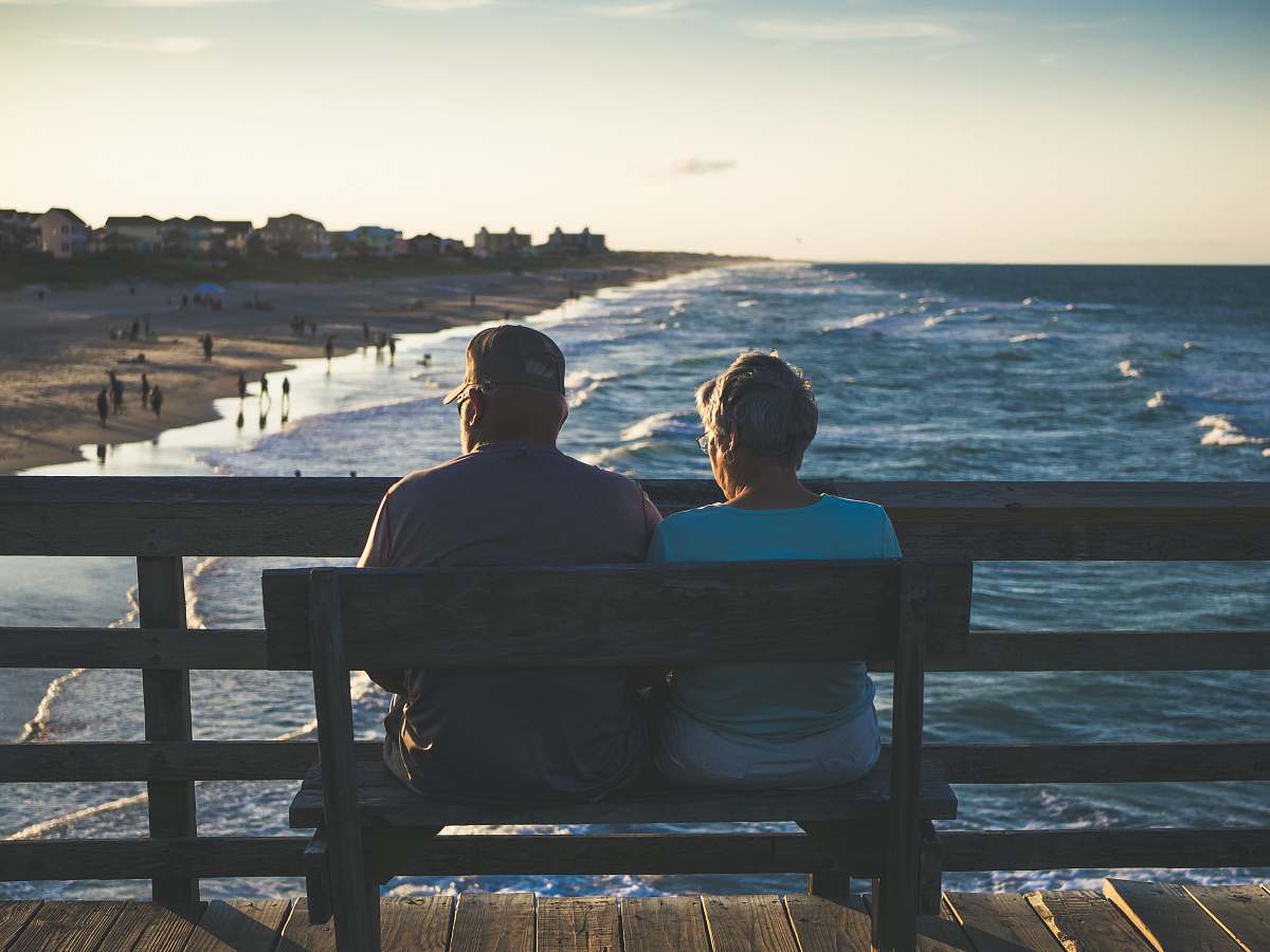 human man and woman sitting on bench in front of beach person