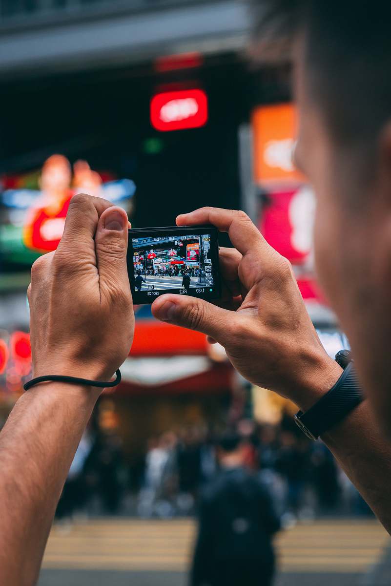 person man capturing several people on street selective focus photo human