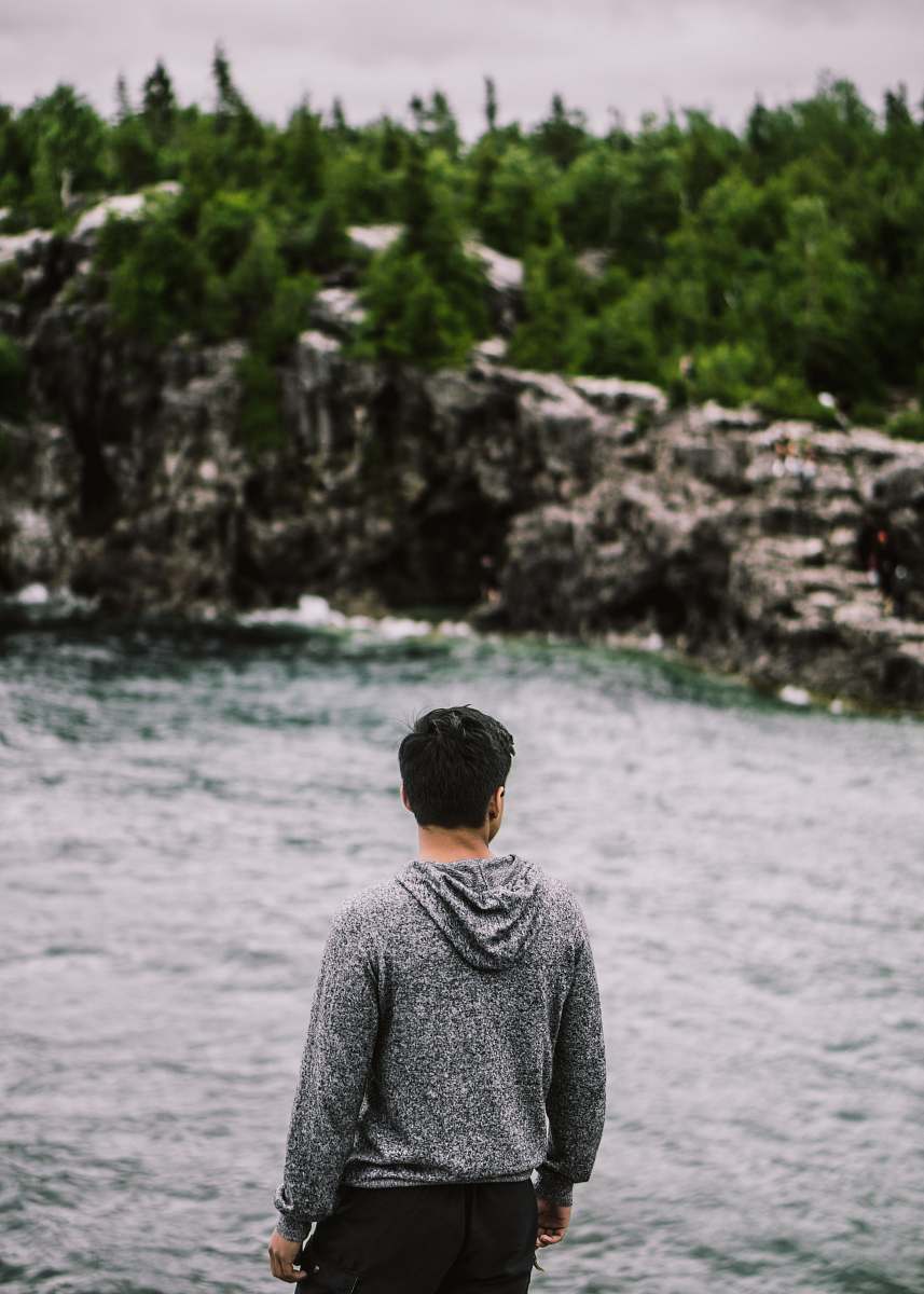 human man facing backward fronting body of water and trees foliage person