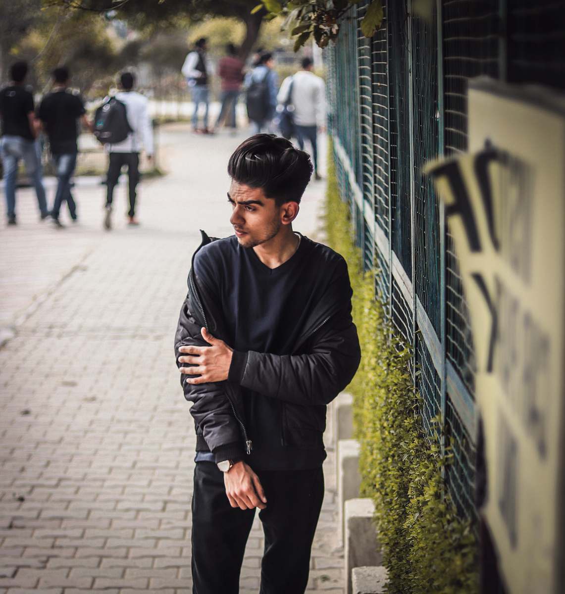 human man in black sweater standing beside blue metal fence during daytime person