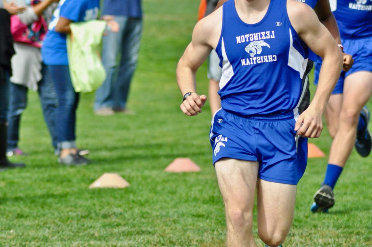 human man in blue Champion tank top and shorts running at the field sports