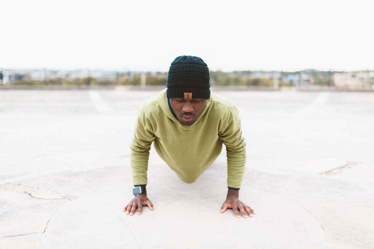 person man in green long-sleeved shirt doing a push-up on gray concrete pavement human