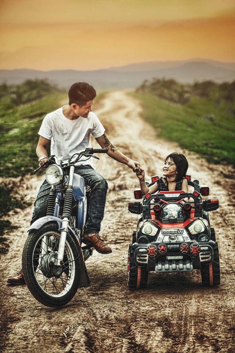 person man riding motorcycle and toddler on a toy car in a road during daytime vehicle