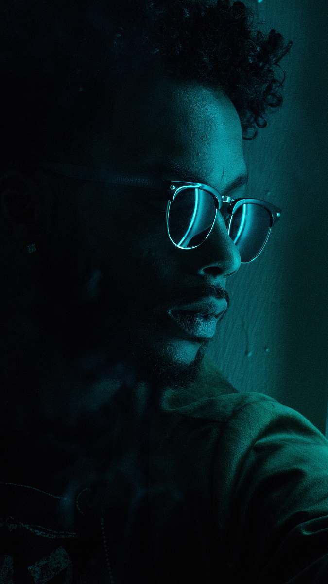 person man sitting near wall wearing black framed sunglasses human