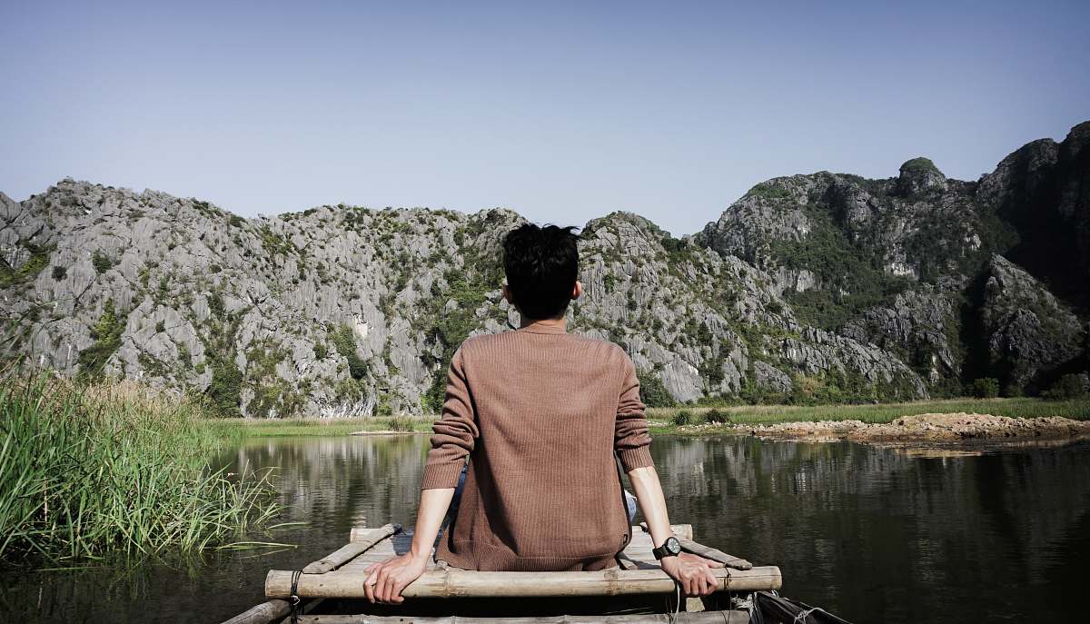 human man sitting on brown dock in front of gray rock formation person