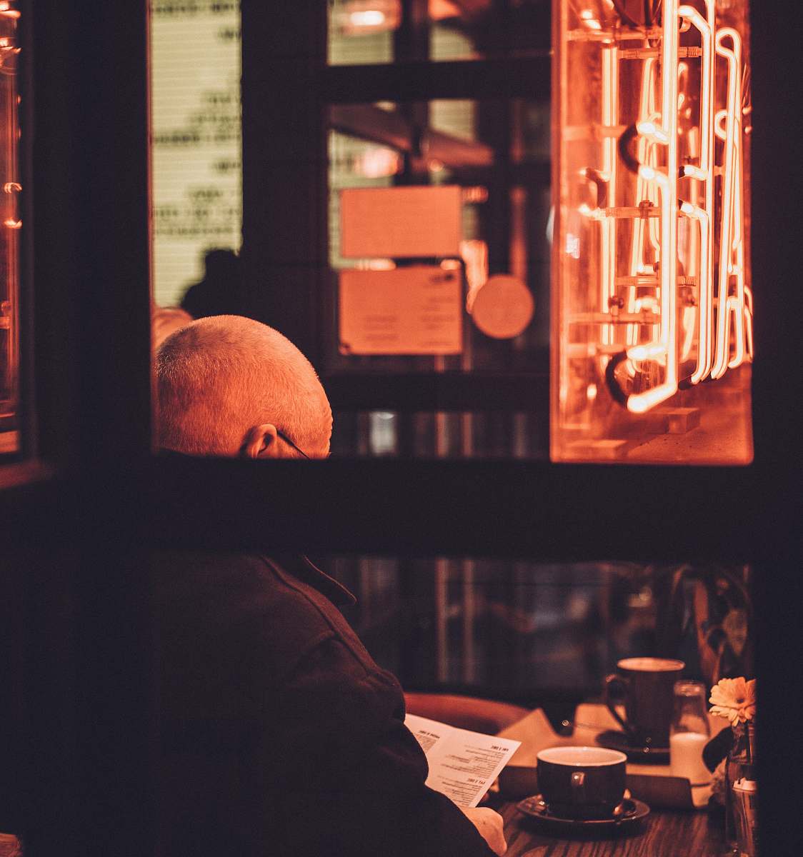 person man sitting on chair reading book in front of table cup