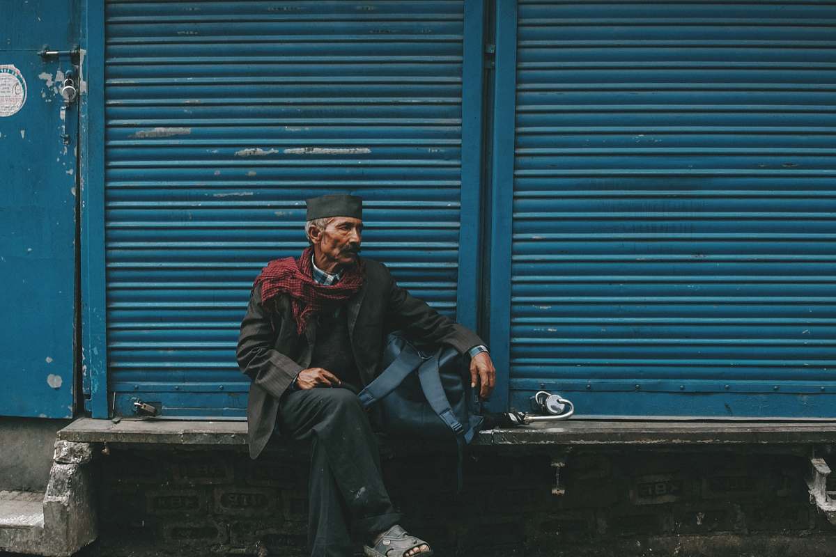 person man sitting on gray bench in front of blue shutter door human