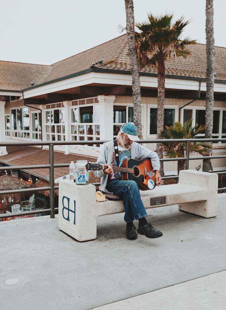guitar man sitting on outdoor bench playing guitar during daytime musician