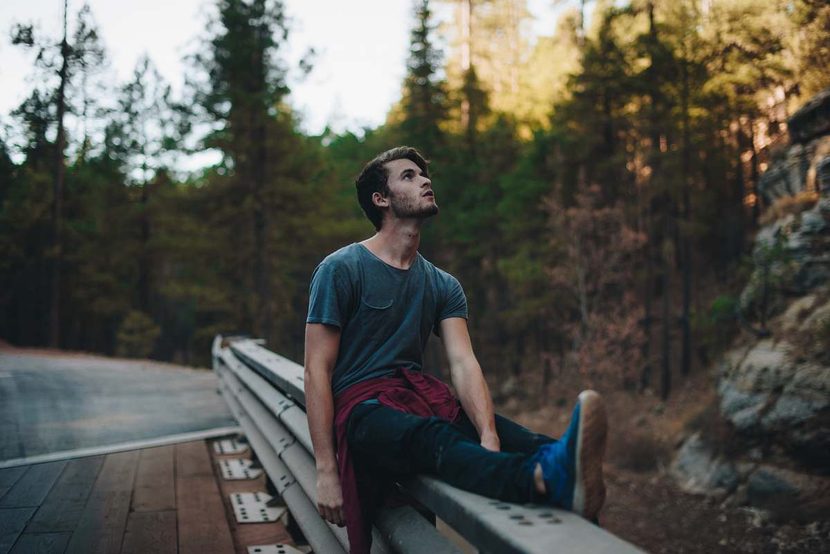 person man sitting on rails looking up during daytime human