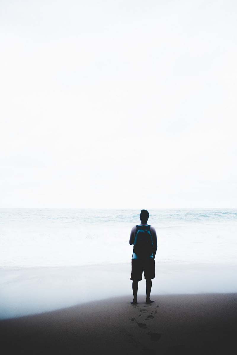person man standing in front of body of water while carrying blue and black backpack human