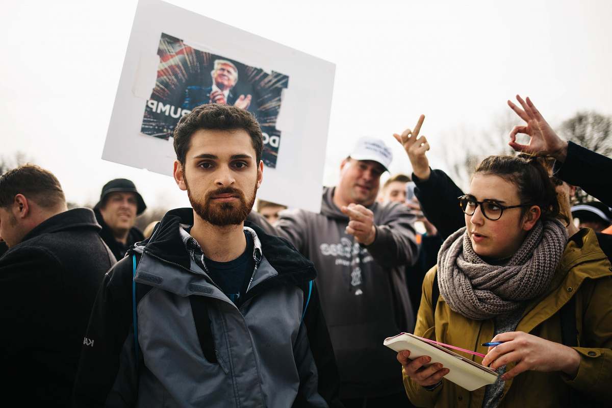 human man standing next to crowd with Donald Trump poster person