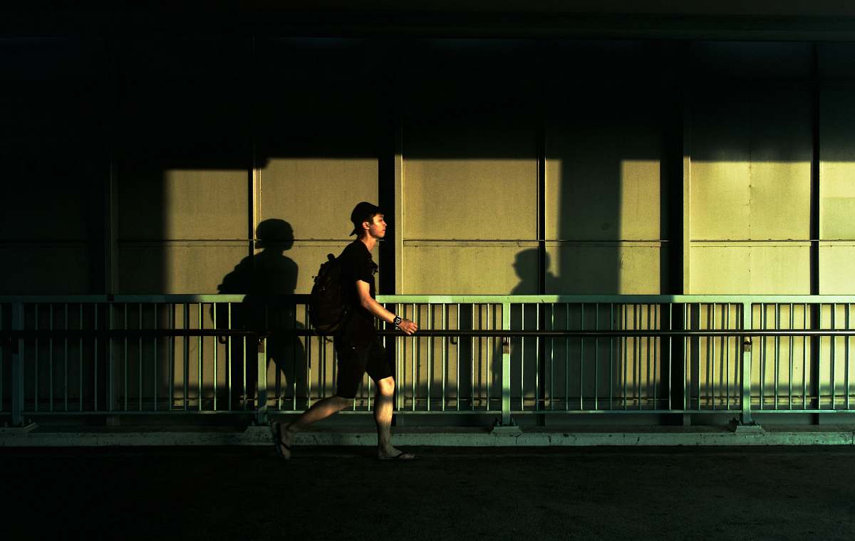 human man walking beside gray metal fence person