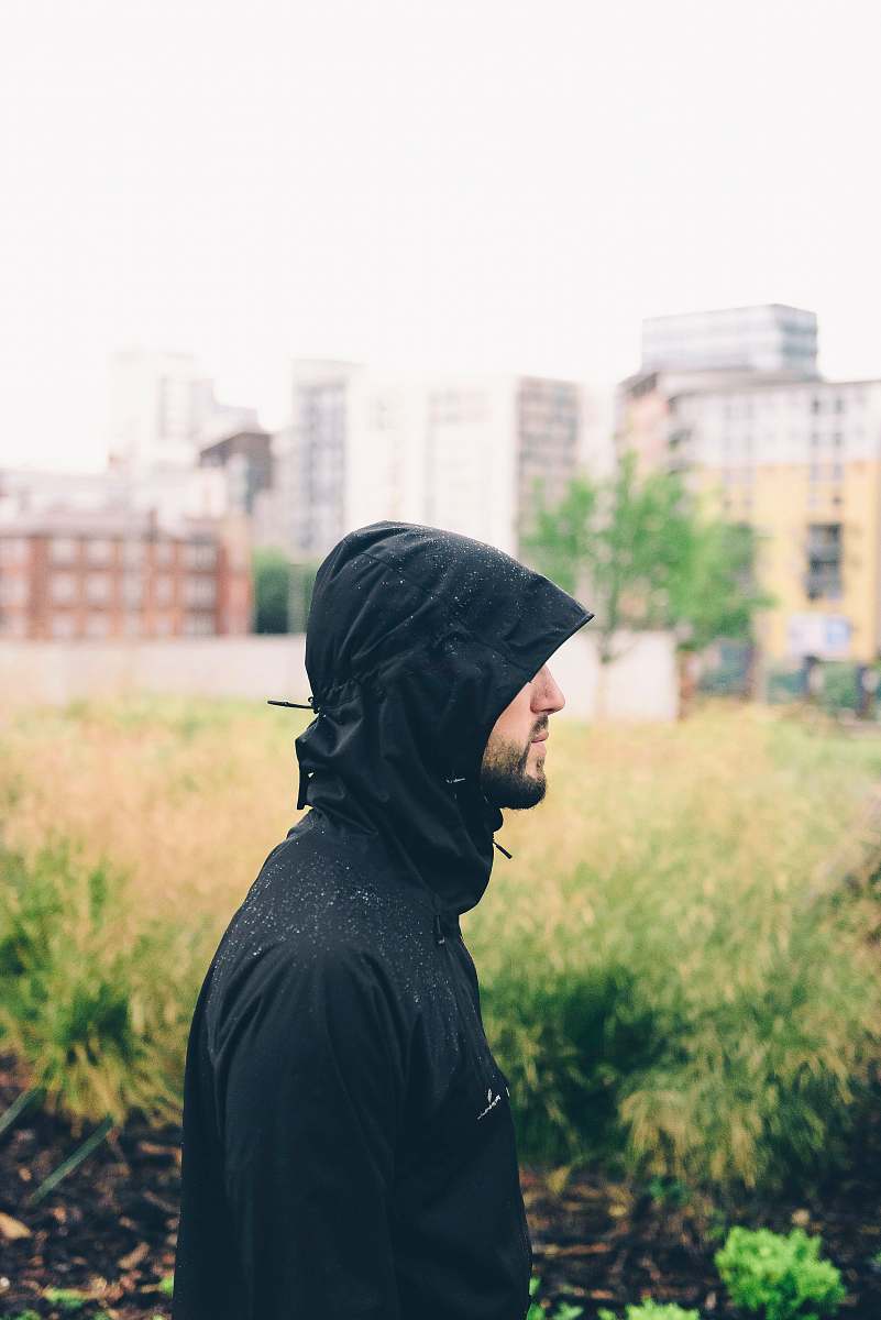 This captivating image features a stylish man dressed in a black hoodie, casually standing amidst lush green grass in a vibrant park setting in Manchester. The background showcases a modern building, offering a contrast between urban life and nature. This scene is perfect for creative projects, lifestyle blogs, and marketing materials that focus on urban fashion, outdoor activities, or contemporary living.