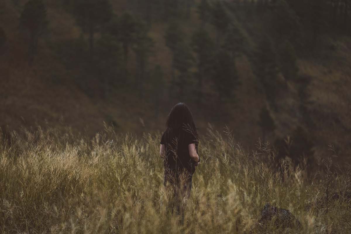 person person in black top surrounded by bushes with trees ahead during daytime grass