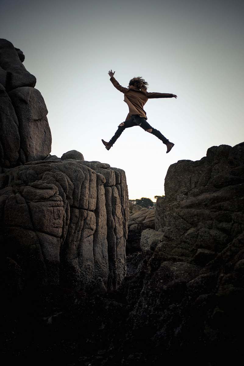 person person jumping on big rock under gray and white sky during daytime rock