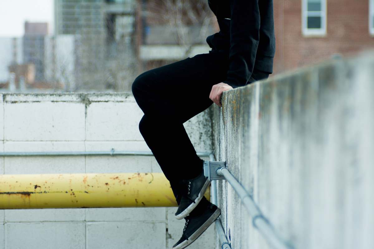 human person sitting on top of white concrete wall near yellow metal pipe person