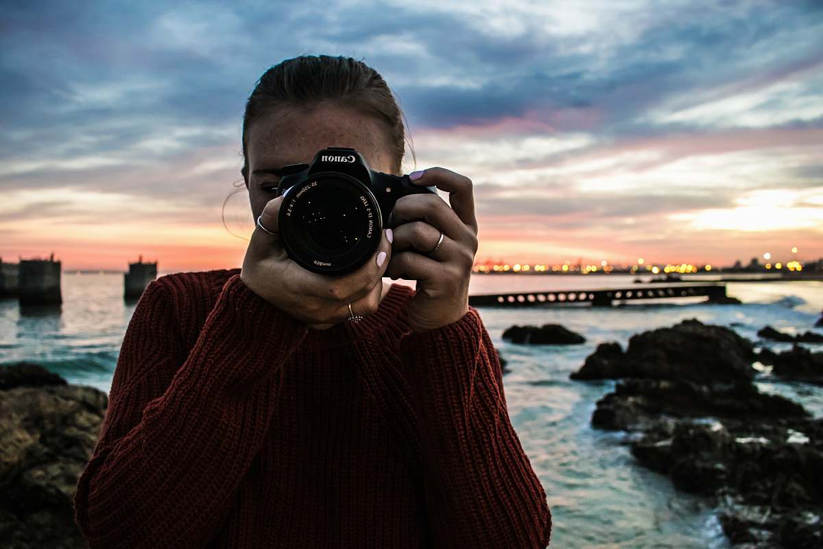 person photo of woman holding black Canon DSLR camera near body of water camera