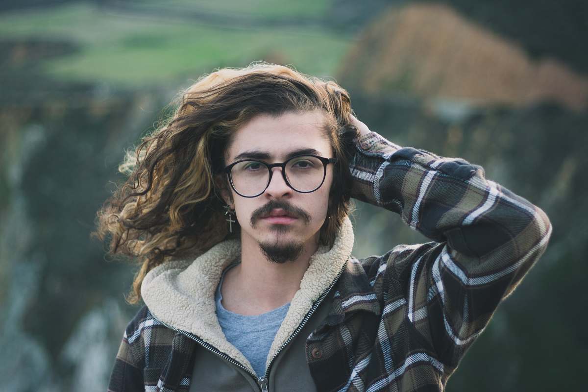 person selective focus photography of man holding his hair wearing black and green zip-up hoodie and crew-neck shirt human