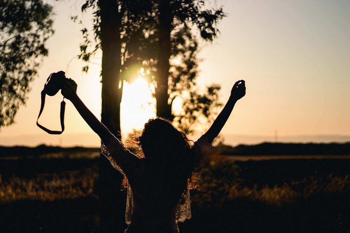 human silhouette photo of woman raising her hands while holding DSLR camera person